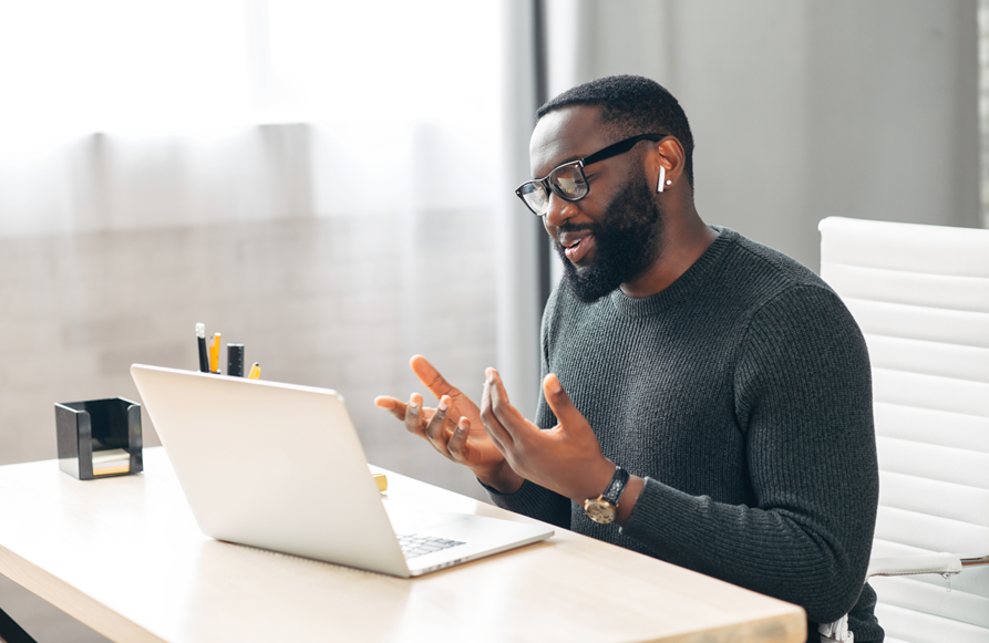 Young African-American man wearing a dark gray sweater and having a virtual conversation with someone using his headset