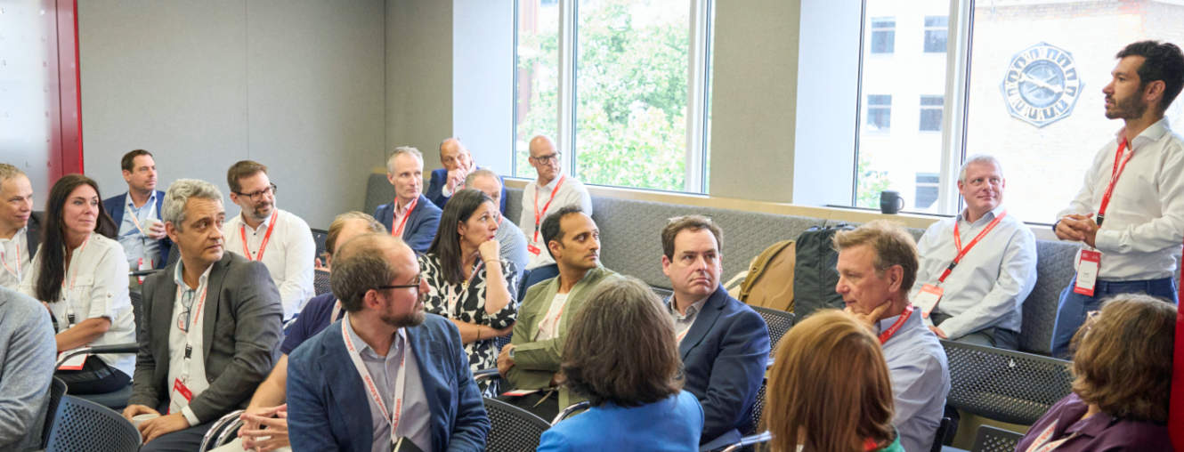 A group of European audience looking at a male speaker in the back of a room