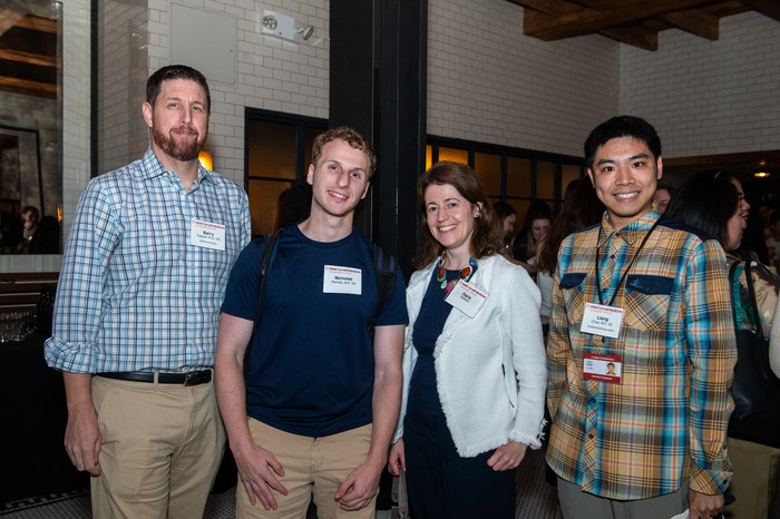 A group of alumni - two men in shirts, one in a navy T-shirt and one woman wearing a white coat