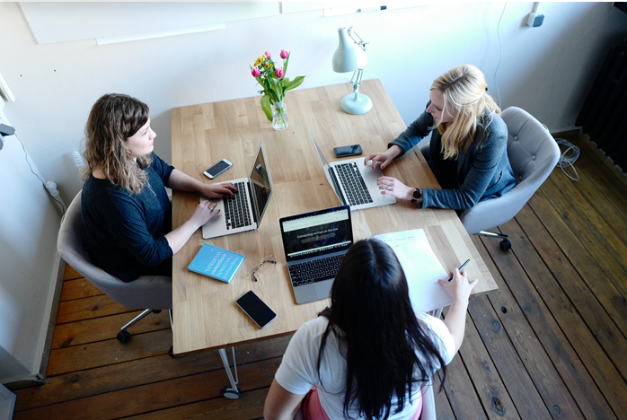 Three young women with laptops sitting at a table having a discussion.