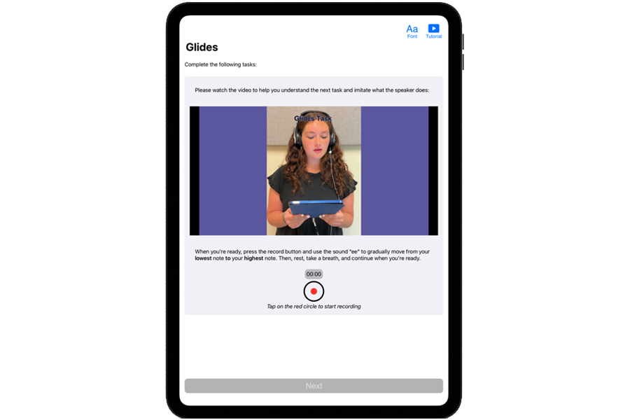 A young woman with curly brunette hair wearing a headset looking at a large blue tablet 