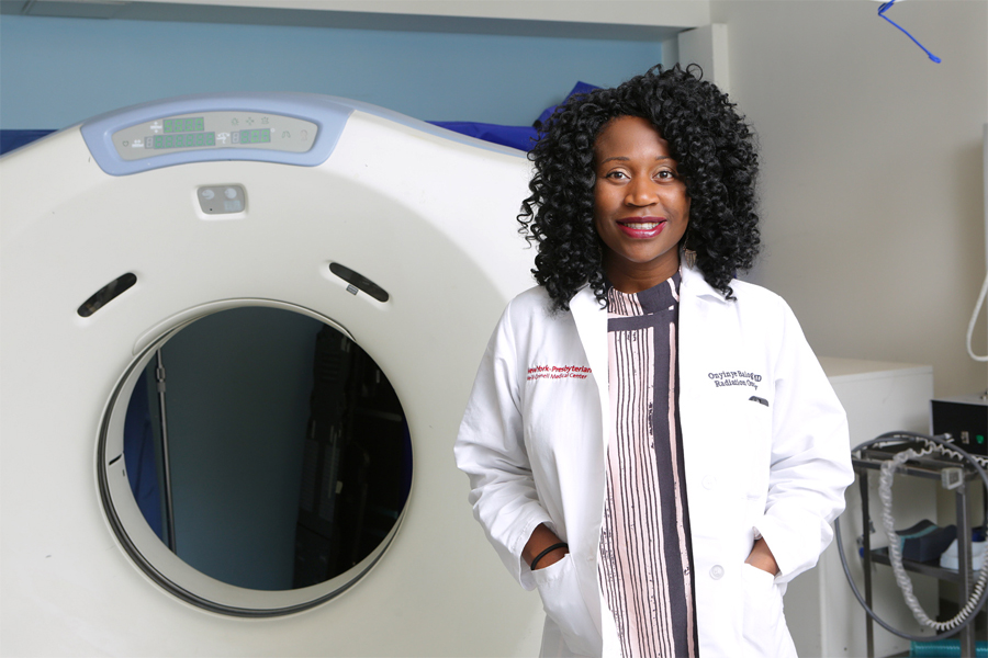 Photo of Dr. Balogun in white coat next to an MRI machine