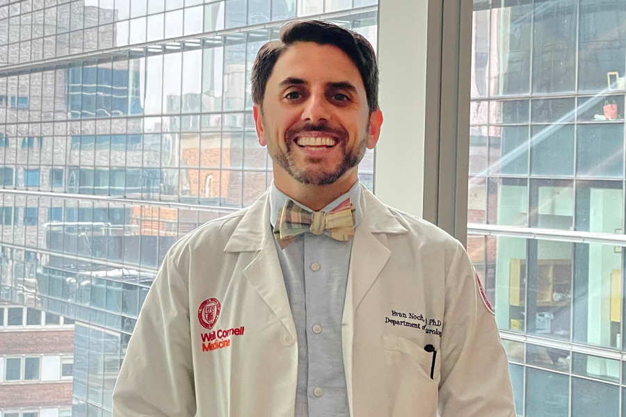 A male doctor wearing a bow tie, blue shirt and white coat who is smiling 