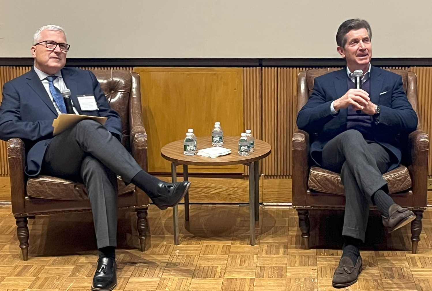 Two Caucasian men in dark-colored business attire sitting on sofas