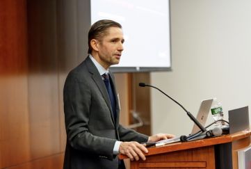 A man in grey suit standing at a podium and talking