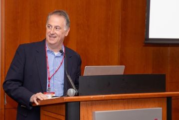 A middle-aged man wearing a blue shirt and suit standing at the podium