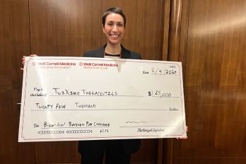 A young Caucasian woman in dark, short hair holding a big check