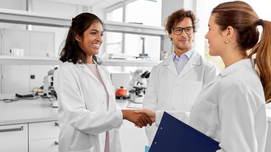 Three doctors (two female and one male) in white coats talking in a lab.