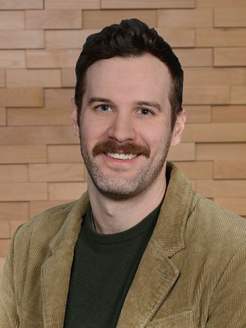 A young Caucasian male with a mustache, wearing a dark green and khaki suit