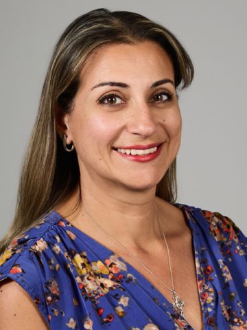 A woman with long brunette hair and wearing a necklace with a cross