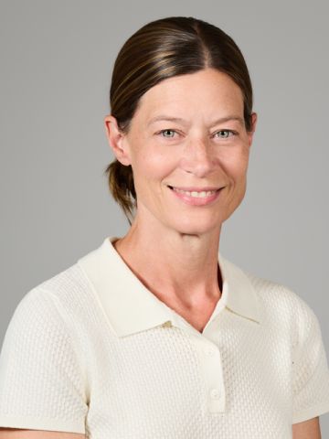 Caucasian woman with brunette hair in a bun, light green eyes and wearing a white shirt