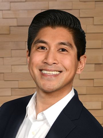 A young Asian man wearing a white shirt and black suit and smiling. 