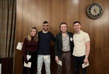 The first-place team of one Caucasian woman, one South Asian man and two Caucasian men holding their prize envelopes.