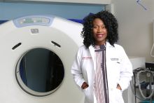 Photo of Dr. Balogun in white coat next to an MRI machine