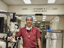 Dr. Spector, a middle-aged Caucasian surgeon wearing a red surgical gown and blue hair net standing in the hall of an operating room