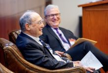 Two older men wearing suits and ties smiling and talking.