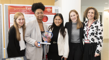 A group of five women of diverse ethnicities. An African-American woman in the middle holding a device prototype.