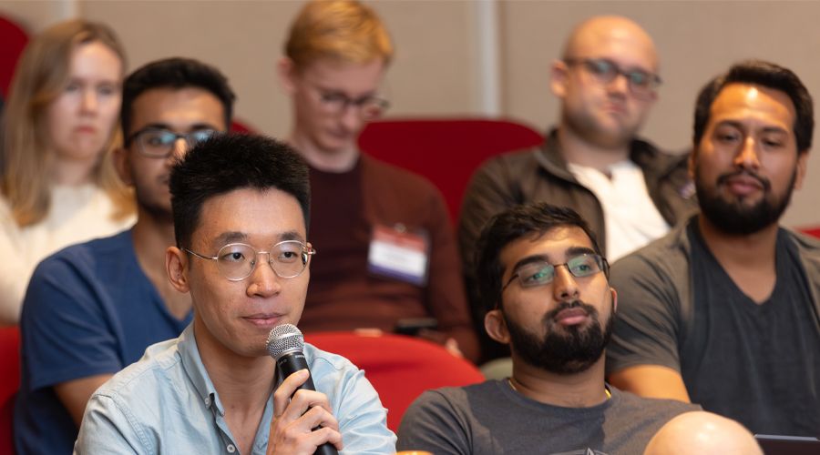 An East Asian male student asking a question in an auditorium full of students