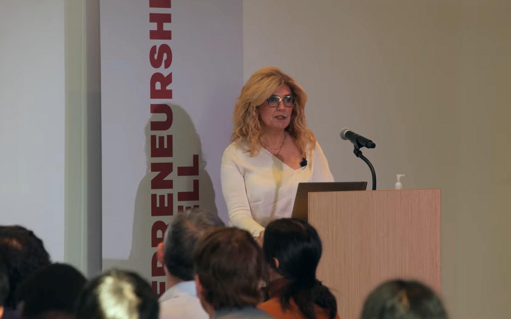 A middle-aged blonde woman wearing glasses presenting to an audience