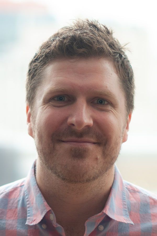 Caucasian man with short brunette hair wearing a shirt with light blue and pink squares