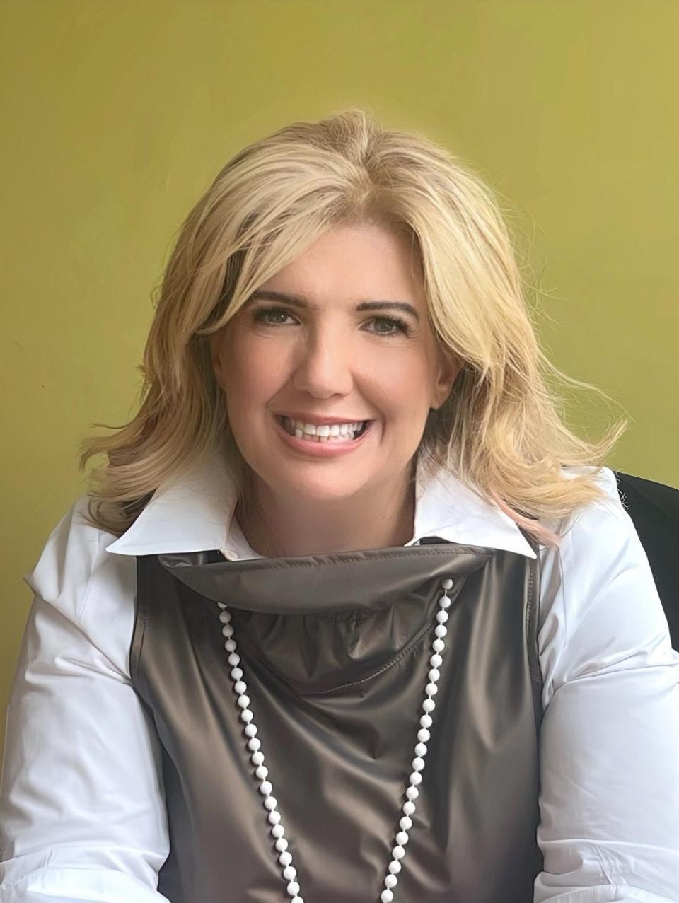 Middle-aged blonde woman wearing a white shirt and pearl necklace