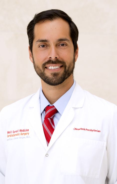 Young male doctor with dark hair and beard wearing a white coat and red tie