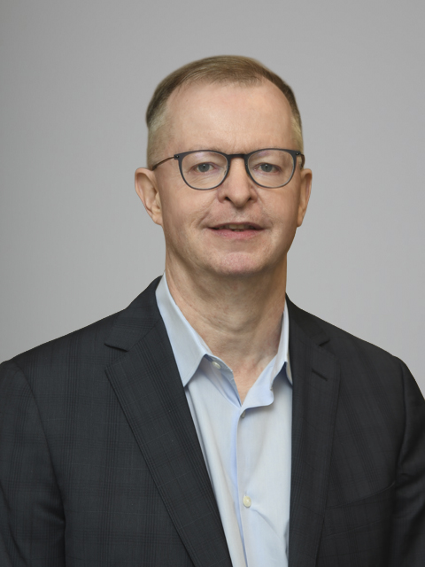 Caucasian man wearing glasses, a light blue shirt and dark gray suit